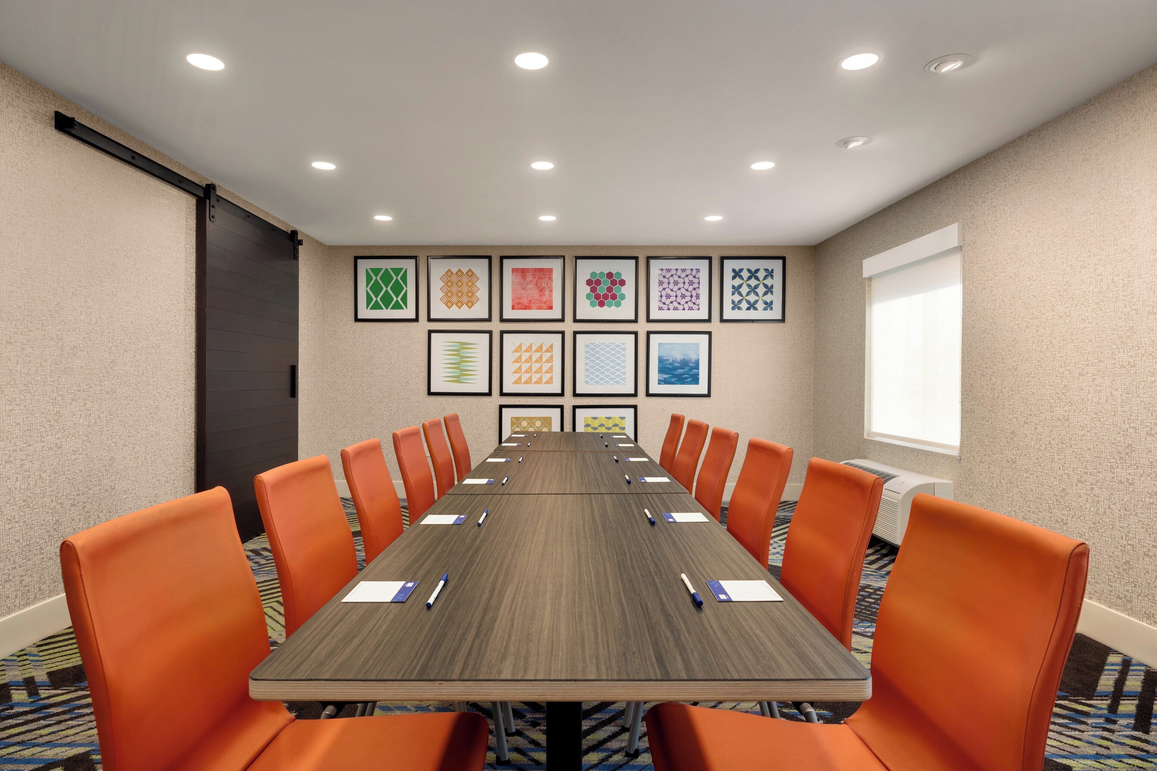 A conference room with a long table, orange chairs, and framed artwork on the walls.