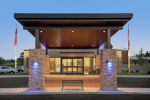 A modern building with a covered entrance, stone pillars, and two American flags. - Holiday Inn Express Plattsburgh by IHG (Plattsburgh)