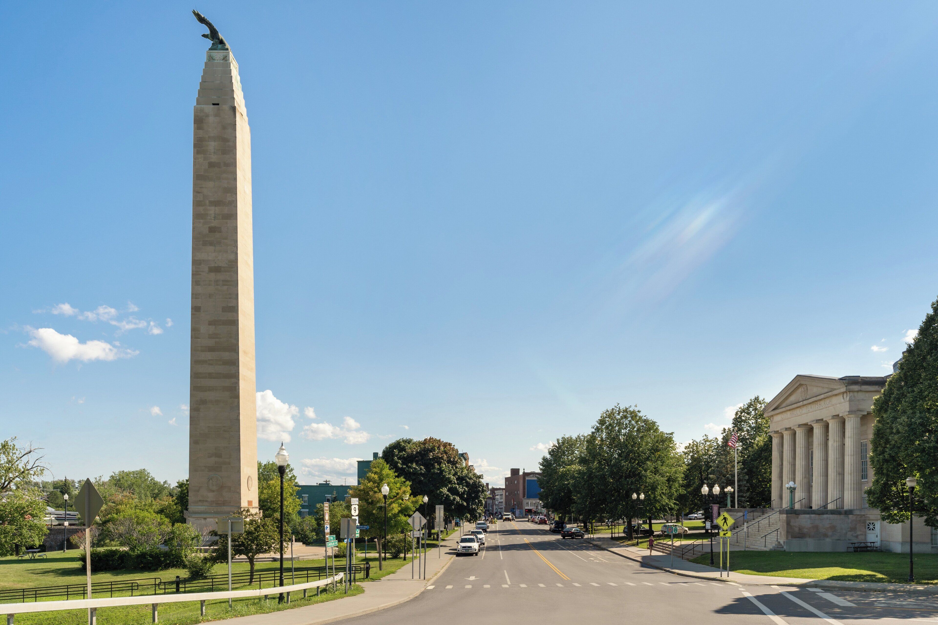 A tall monument with a statue on top, a road with cars, and a building with columns.