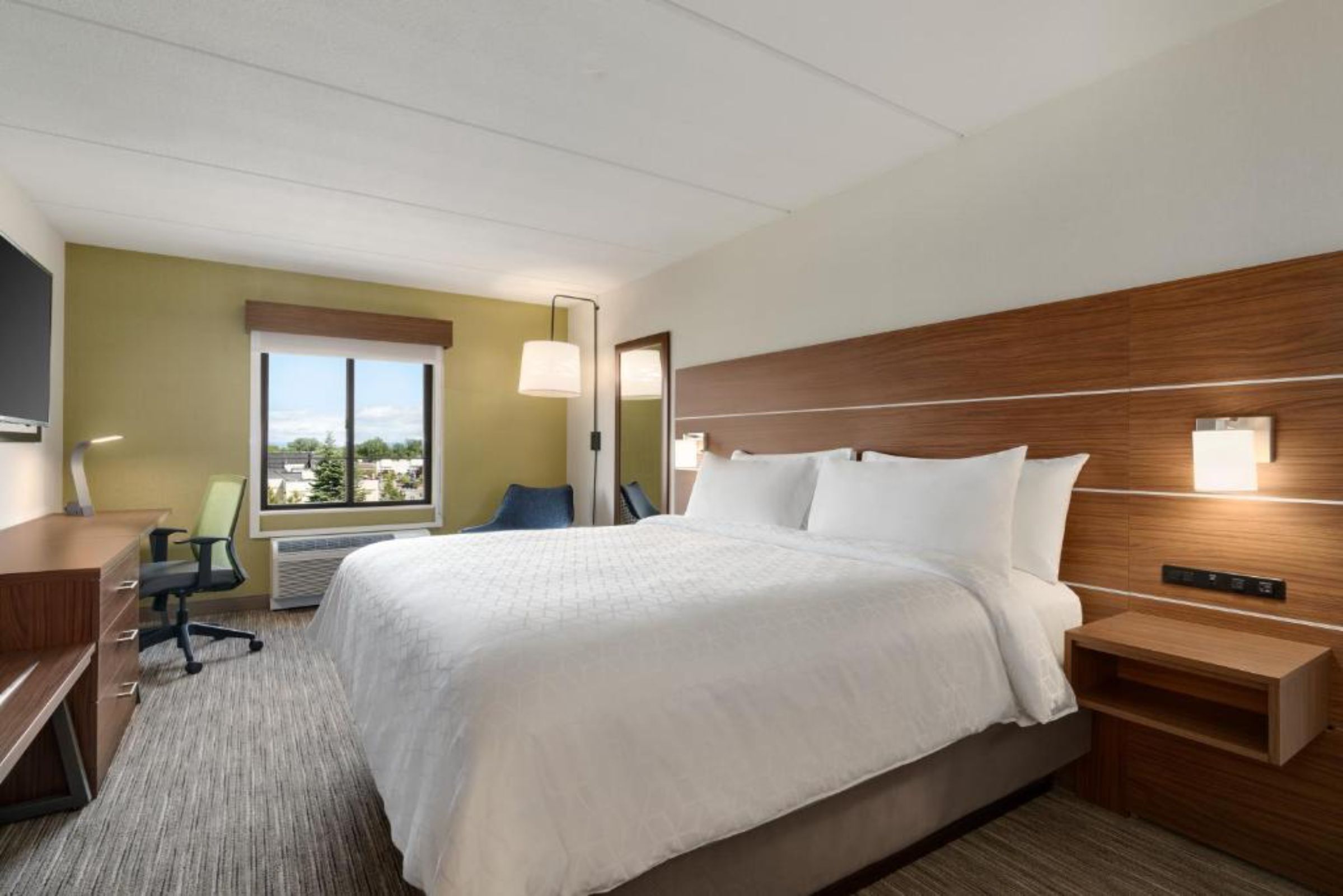 A hotel room with a large bed, a desk, a chair, a TV, and a window with a view.
