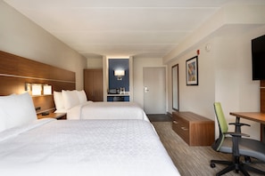 A hotel room with two beds, a desk, a chair, a TV, and a kitchenette.