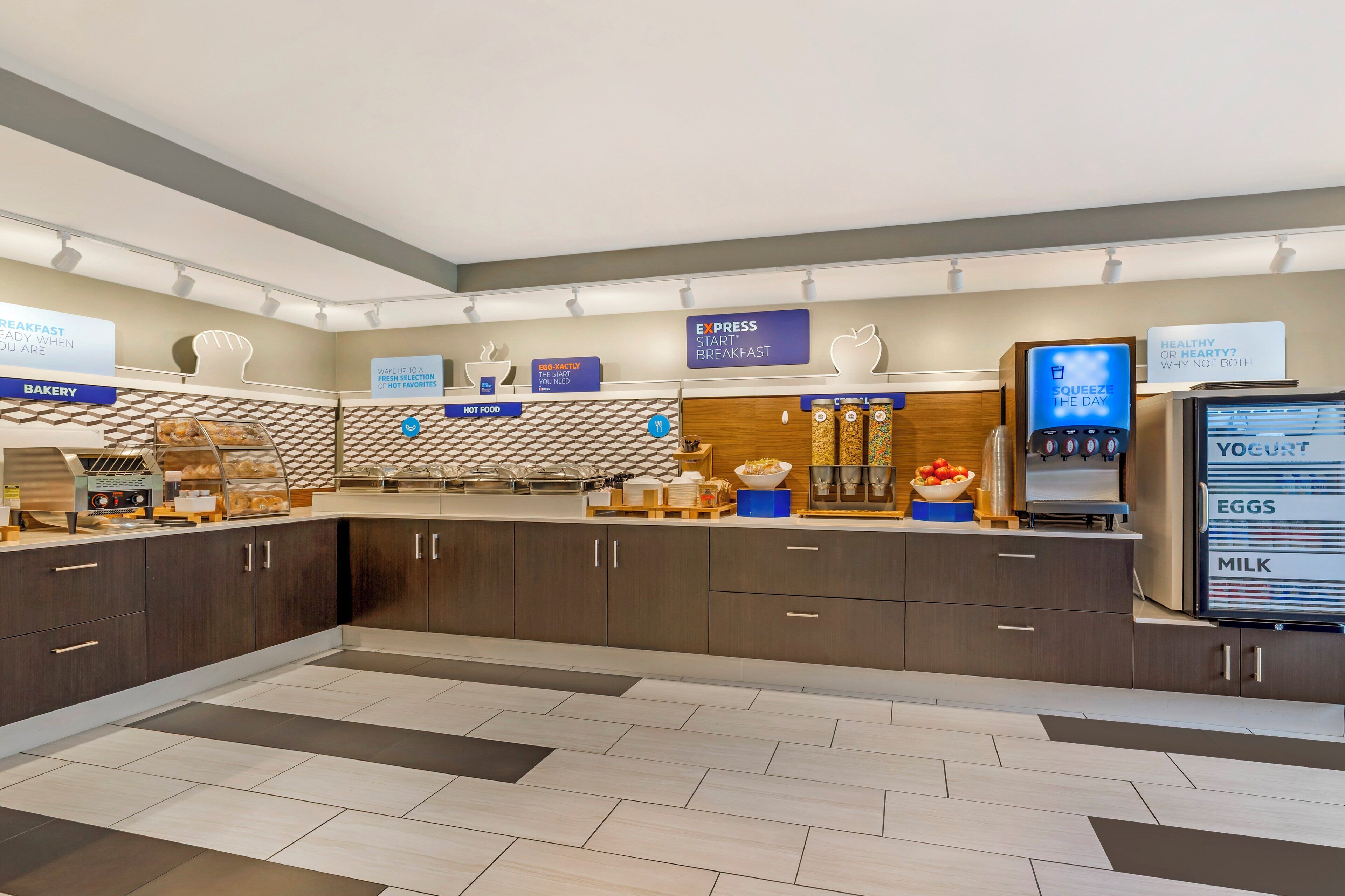 Espaço moderno para o café da manhã, com padaria, estação de comida quente e dispensador de iogurte.
