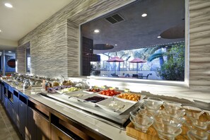 A buffet with various food items and glassware, set against a backdrop of a modern interior with a view of outdoor seating. - DoubleTree by Hilton Phoenix North (Phoenix)