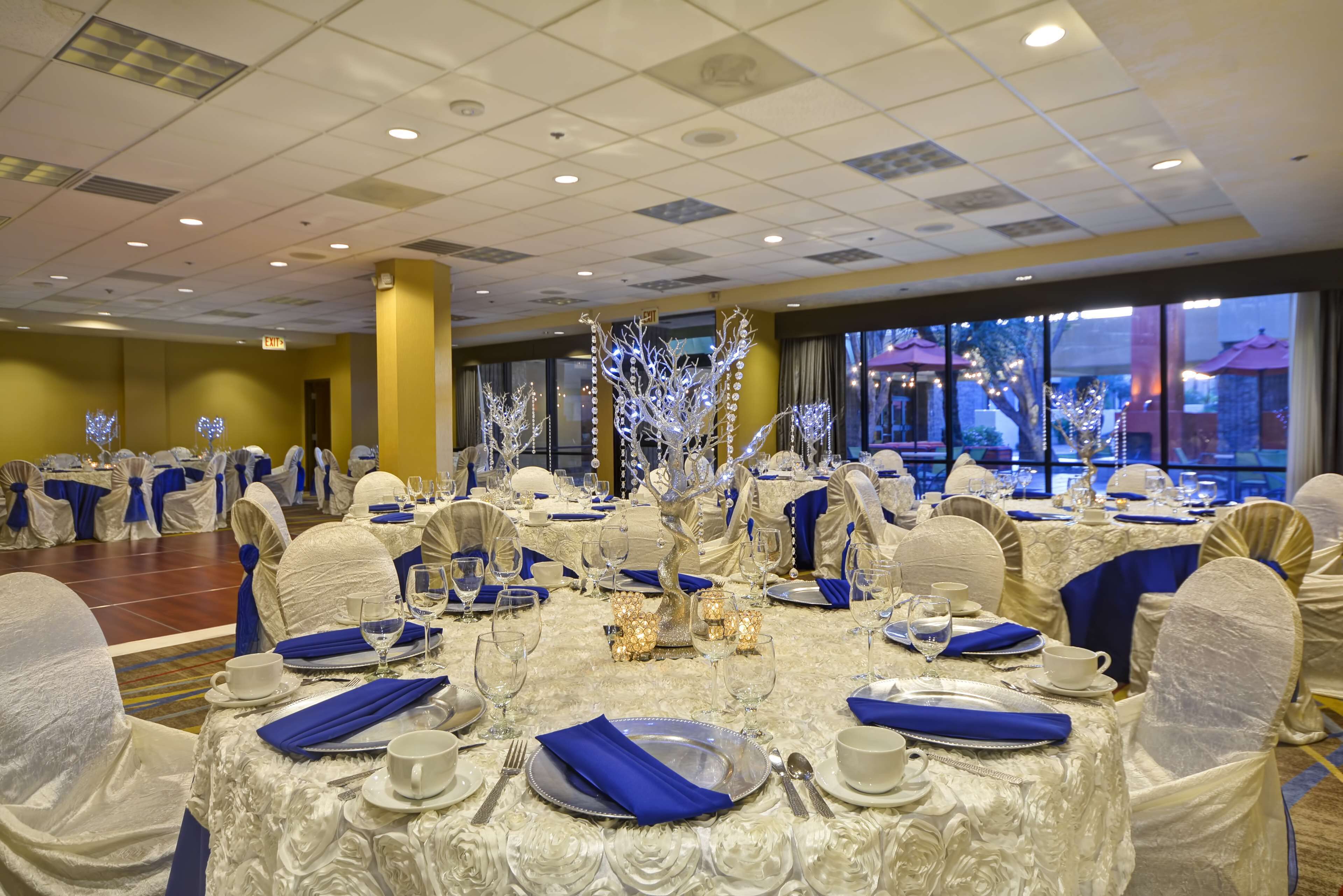 A banquet hall with round tables set for a formal event, featuring white tablecloths, blue napkins, and silverware.