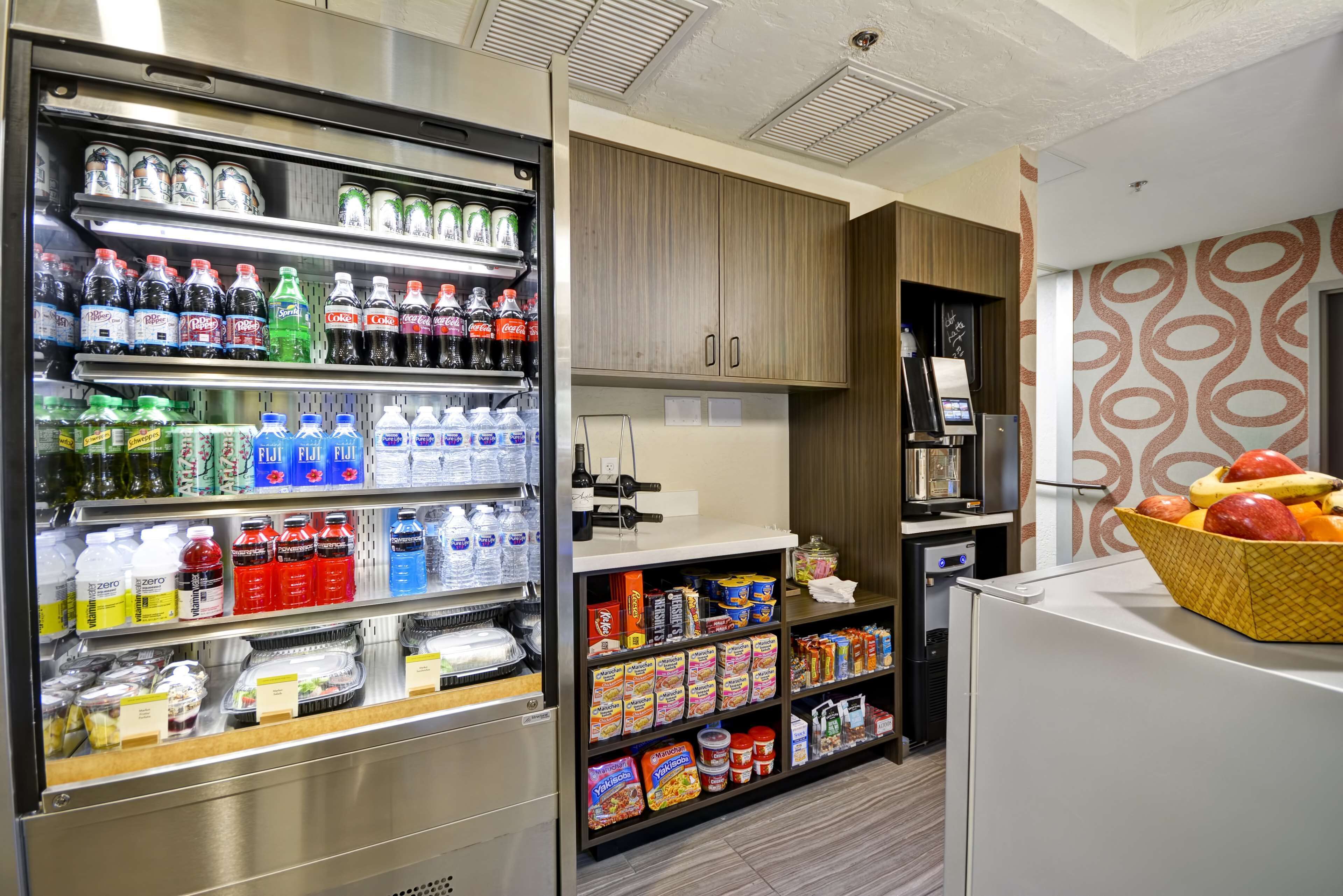 A self-service beverage and snack station with refrigerated drinks, bottled water, and various snack options.