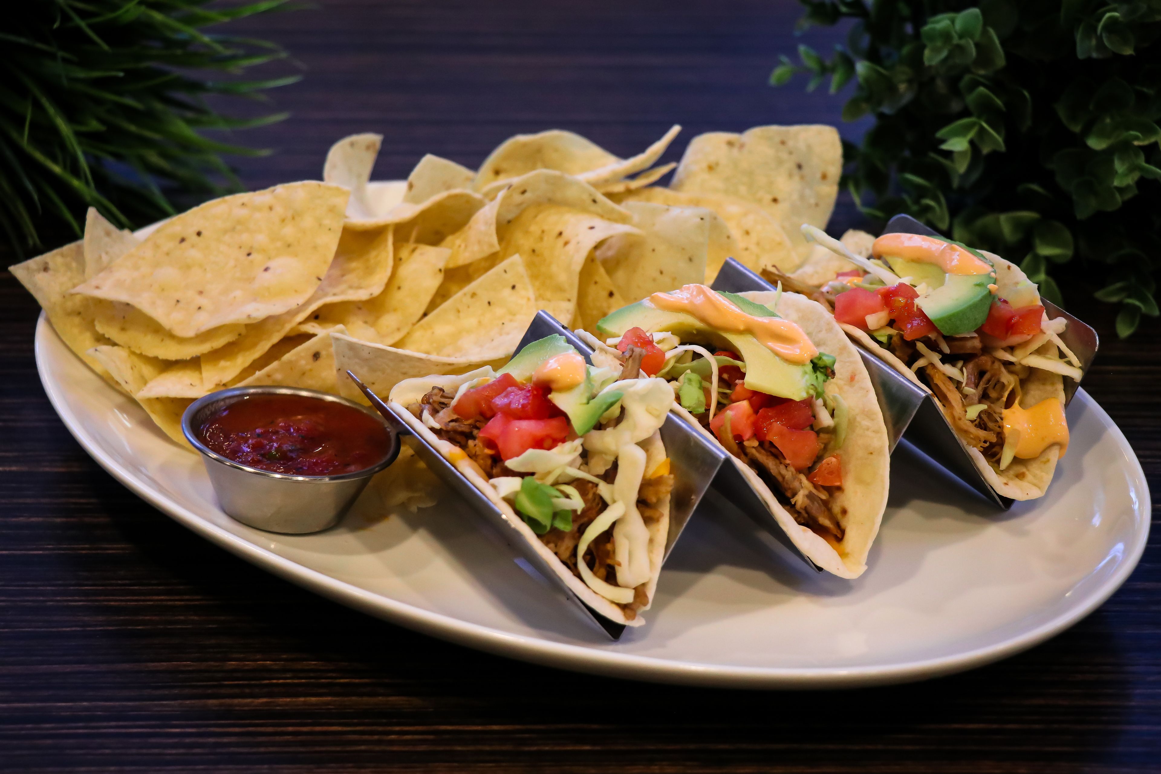 Un plato con tres tacos, un tazón de totopos y un recipiente pequeño de salsa.