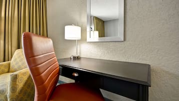 A hotel room with a brown leather chair, a desk with a lamp, and a mirror on the wall.