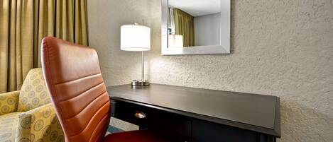 A hotel room with a brown leather chair, a desk with a lamp, and a mirror on the wall.