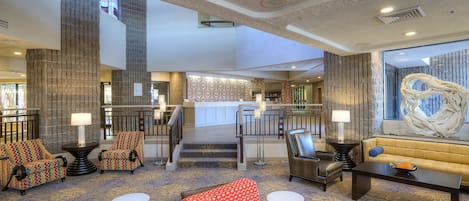 A spacious lobby with a high ceiling, a staircase leading to an upper level, and a variety of seating arrangements including sofas and armchairs.