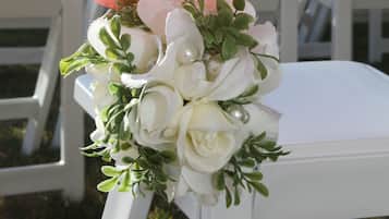 Ein weißer Stuhl mit einem rosafarbenen Band und einem Blumenstrauß aus weißen Blüten.
