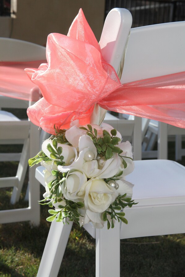 A white chair with a pink ribbon and a bouquet of white flowers.