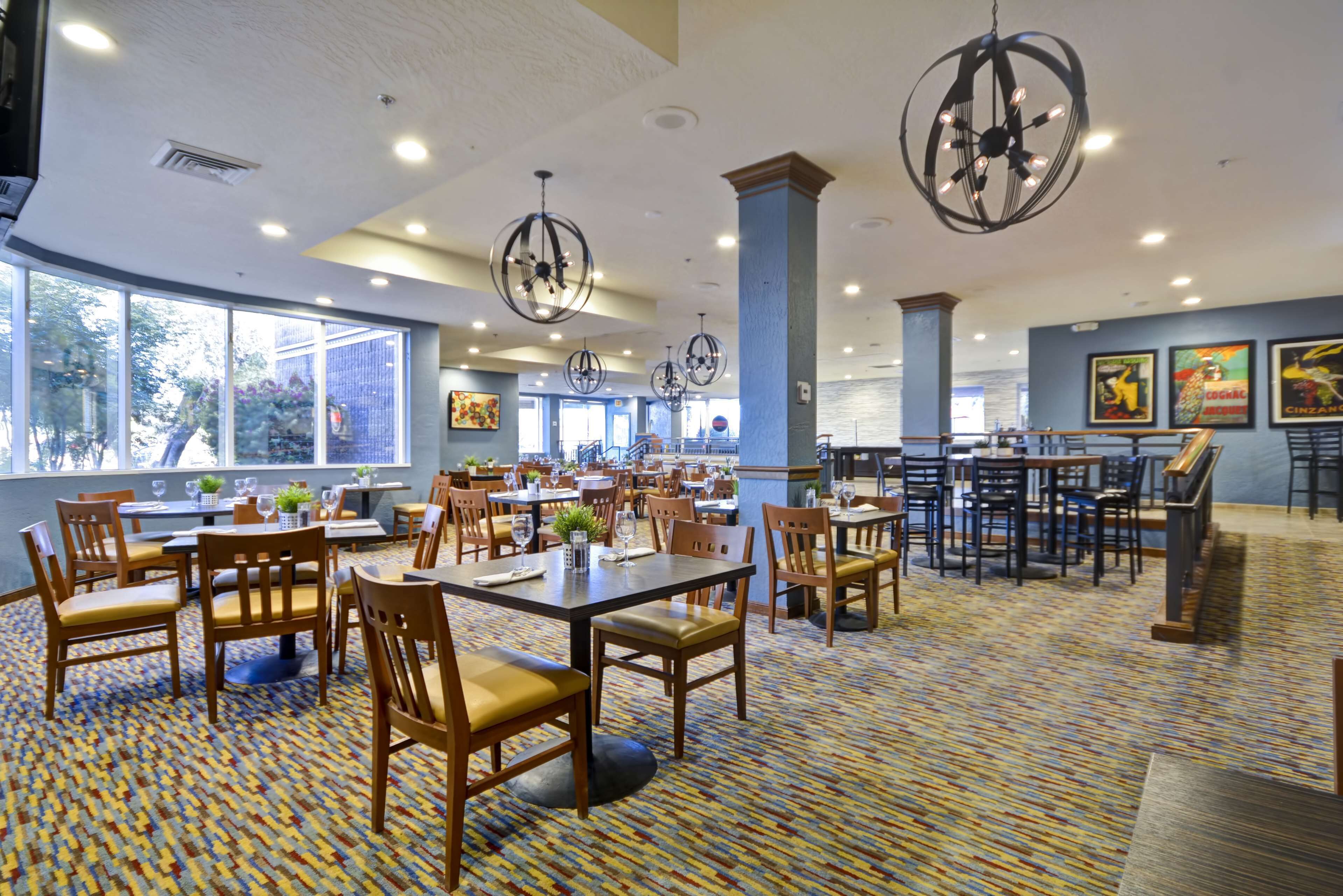 A spacious dining area with multiple tables and chairs, large windows, and decorative ceiling lights.