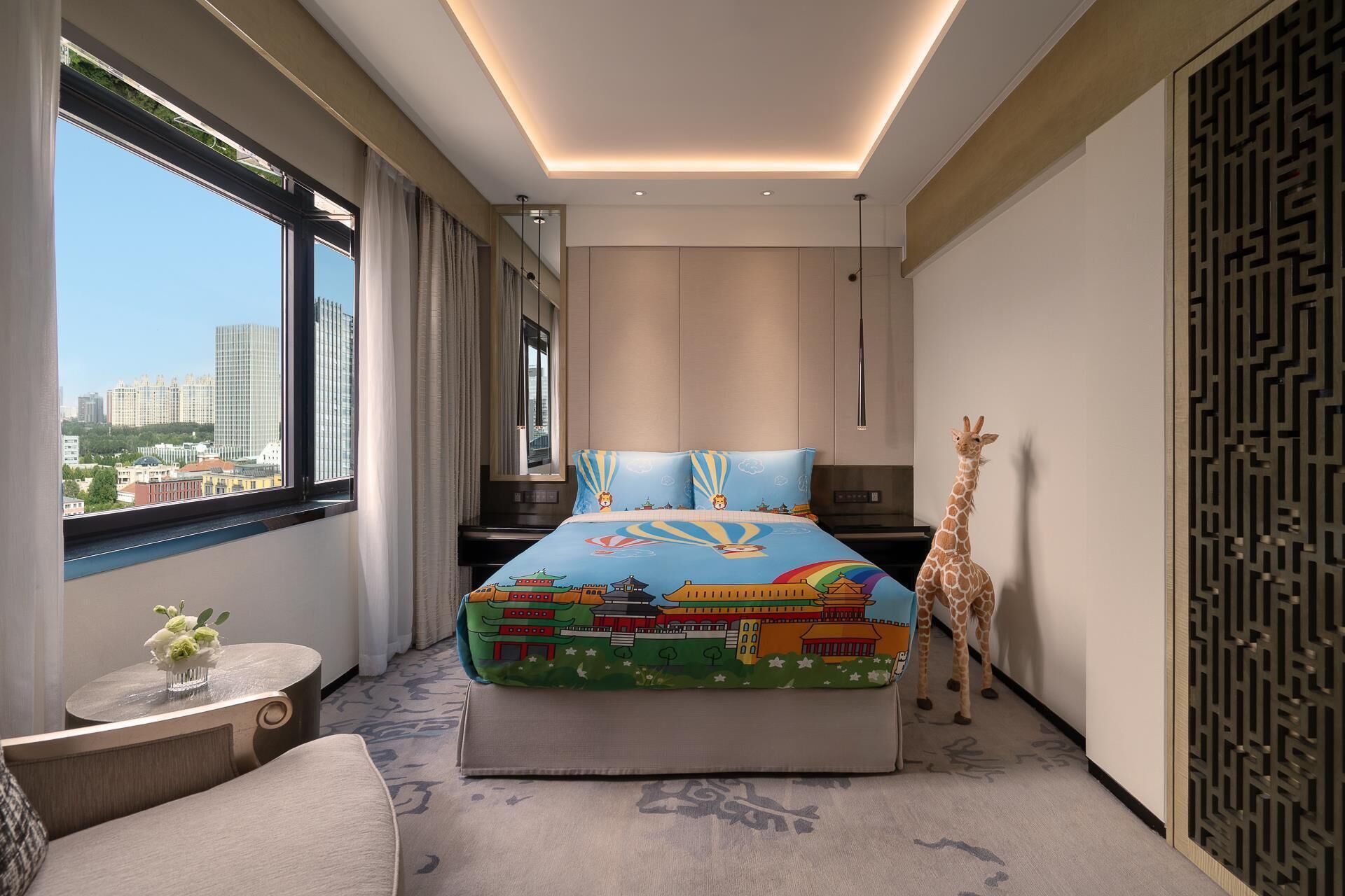 A modern hotel room with a large bed, a view of the city, a giraffe statue, and a decorative wall panel.