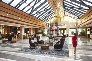 A spacious lobby with a high ceiling and skylights, featuring a reception area, seating arrangements, and a central decorative plant display. - (Beijing)