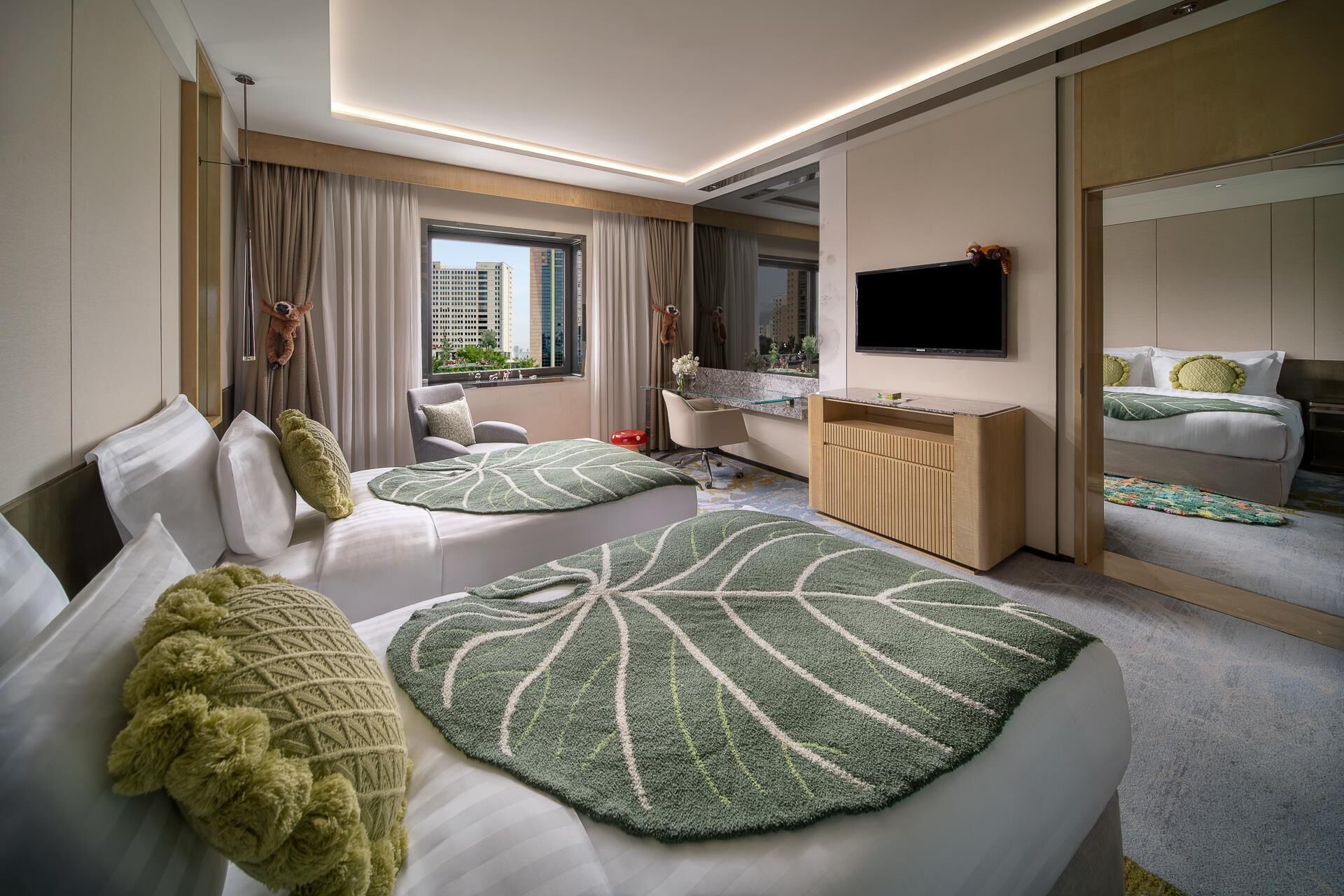 A modern hotel room with two beds, a TV, a desk, and a view of the city.