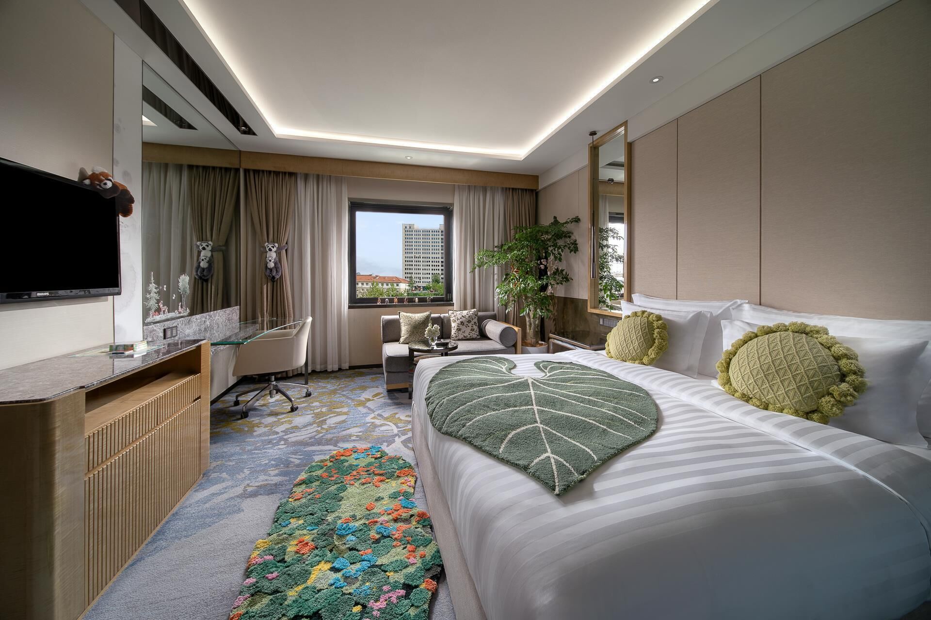 Habitación de hotel con cama, escritorio, televisor, ventana y vista a la ciudad, además de una planta.