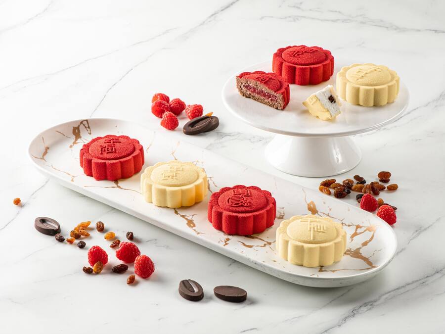 Uma travessa de sobremesas com bolos da lua vermelhos e amarelos sobre uma mesa de mármore branco.