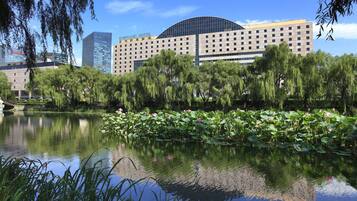 A hotel with a modern design, a large pond with lotus flowers, and a bridge in the background.
