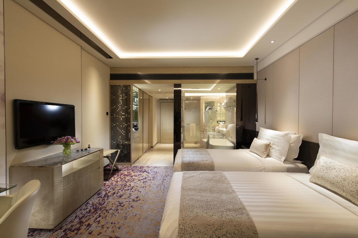 Une chambre d’hôtel moderne dotée d’un grand lit, d’un téléviseur à écran plat, d’un bureau agrémenté d’un vase et d’un dressing.