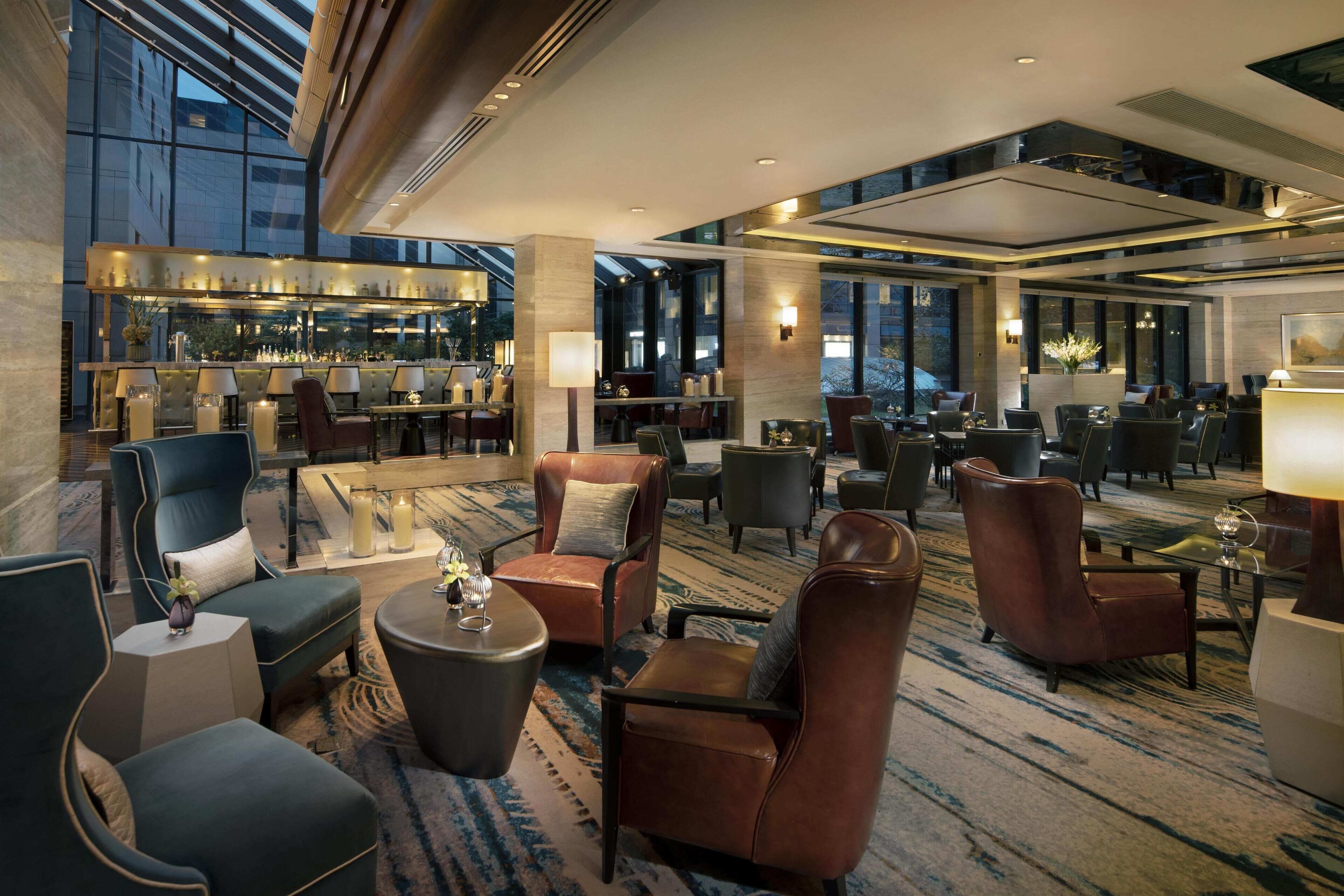 A spacious lobby with multiple seating areas, a bar, and large windows providing views of the outside.