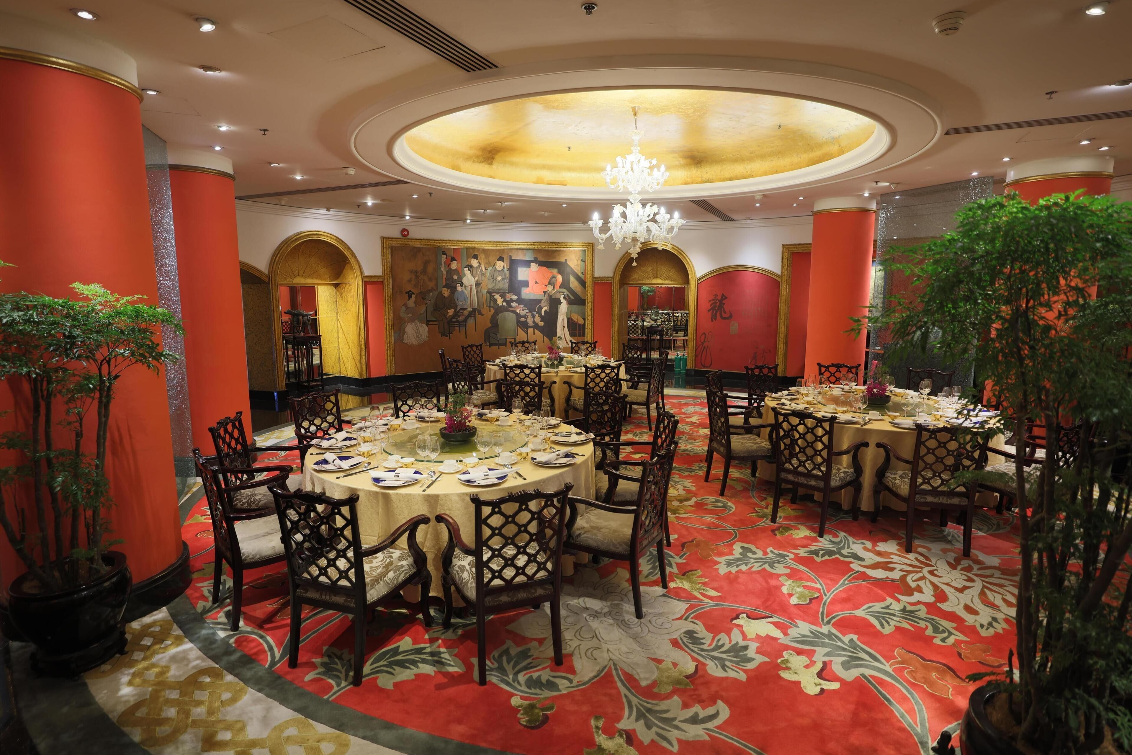 A hotel dining area with round tables, chairs, and a chandelier.