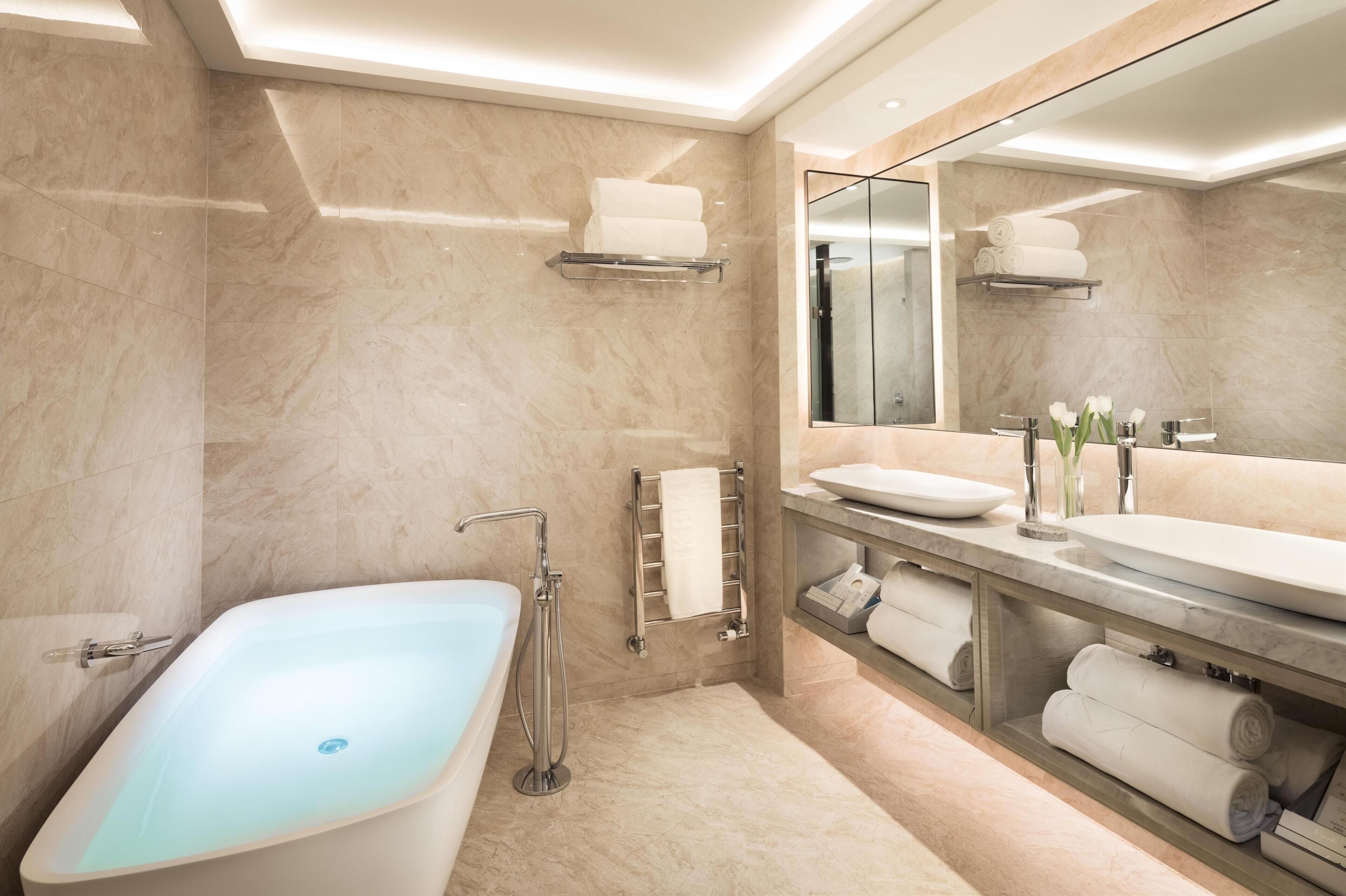 Un baño moderno con una bañera independiente, un espejo grande y estantes empotrados para toallas.