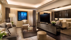 A modern hotel room with a large flat-screen TV, a sofa, a coffee table, and a view of the cityscape. - Kempinski Hotel Beijing Yansha Center (Beijing)