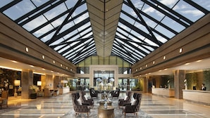 A spacious lobby with a high ceiling and a glass roof, featuring a central seating area with sofas and a coffee table, and reception desks on either side. - Kempinski Hotel Beijing Yansha Center (Beijing)