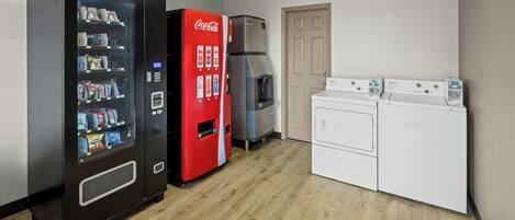 Une buanderie équipée d’un distributeur automatique, d’un réfrigérateur et d’un appareil combinant lave-linge et sèche-linge.