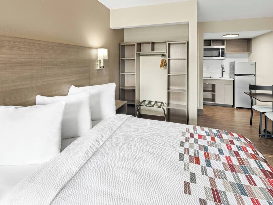 Una habitación de hotel con cama, colcha, armario, escritorio y kitchenette.