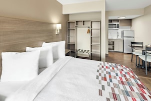 Una habitación de hotel con cama, colcha, armario, escritorio y kitchenette.