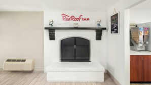 A room with a white brick fireplace, a Red Roof Inn sign, a wall-mounted air conditioner, and a breakfast bar with cereal boxes.