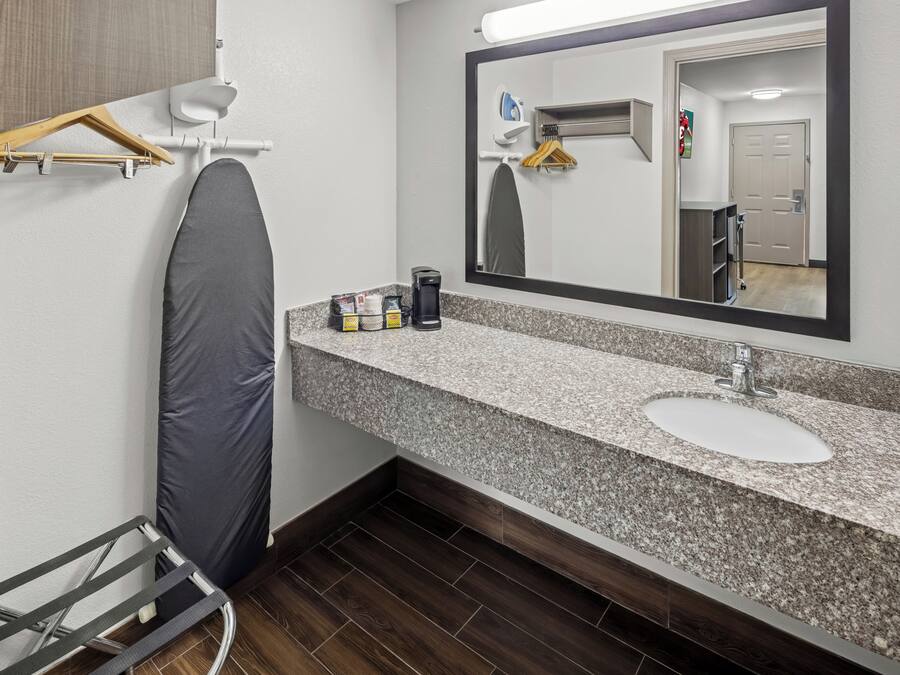 Un baño con encimera de granito, lavamanos, espejo, ducha y toallero.