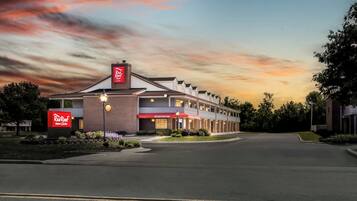 Un hotel Red Roof Inn con fachada de ladrillo, una zona de recepción y un estacionamiento.