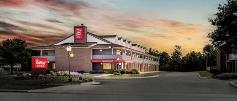 Un hotel Red Roof Inn con fachada de ladrillo, una zona de recepción y un estacionamiento.