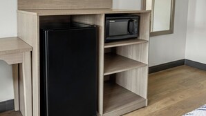 A kitchen with a black refrigerator and a microwave on a wooden shelf.