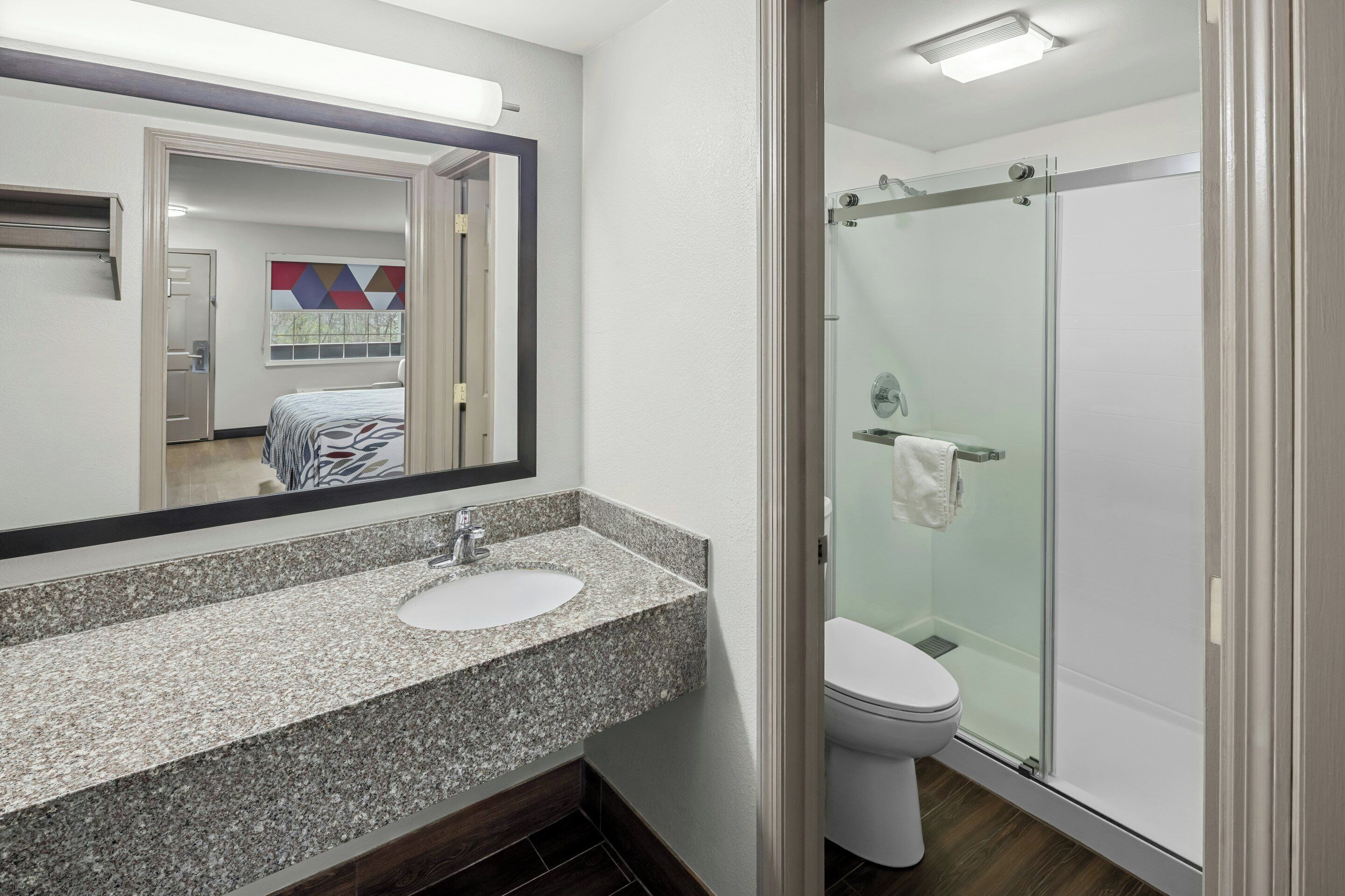 A modern bathroom with a granite countertop sink, a glass shower enclosure, and a visible door leading to another room.