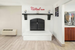 A modern living room with a white fireplace, a mounted sign reading 'Red Roof Inn,' and a beverage dispenser on the right. - Red Roof Inn & Suites Marysville (Marysville)