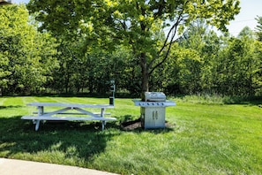 A picnic table and a barbecue grill in a grassy park area with trees in the background. - Red Roof Inn & Suites Marysville (Marysville)