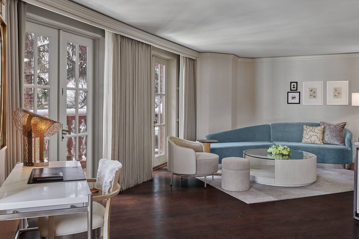 A modern living room with a blue sofa, white armchairs, a glass coffee table, and a dining area with a white table and chairs.