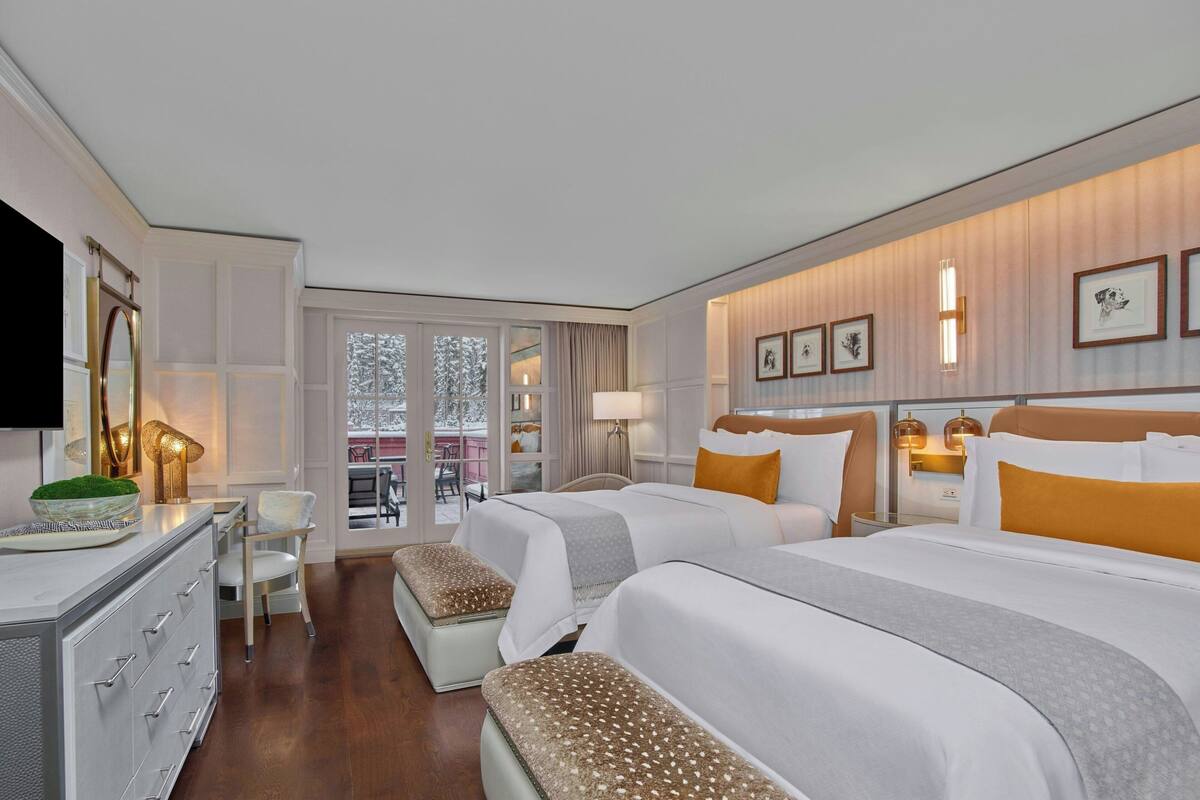 A hotel room with two beds, a desk, and a seating area with a view of the outdoors.