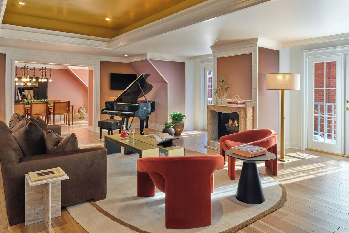A spacious living room with a grand piano, a fireplace, and a dining area in the background.