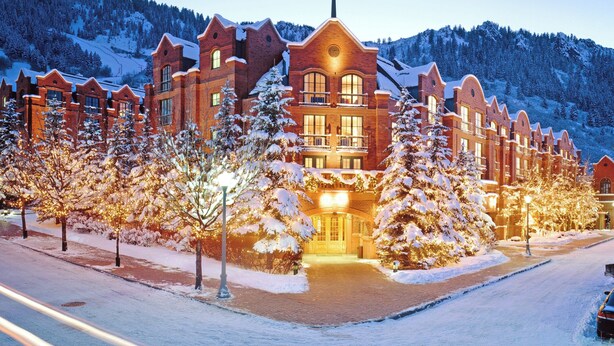A large, multi-story hotel with a prominent central tower, surrounded by snow-covered trees and a mountainous backdrop. - The St. Regis Aspen Resort (Aspen)