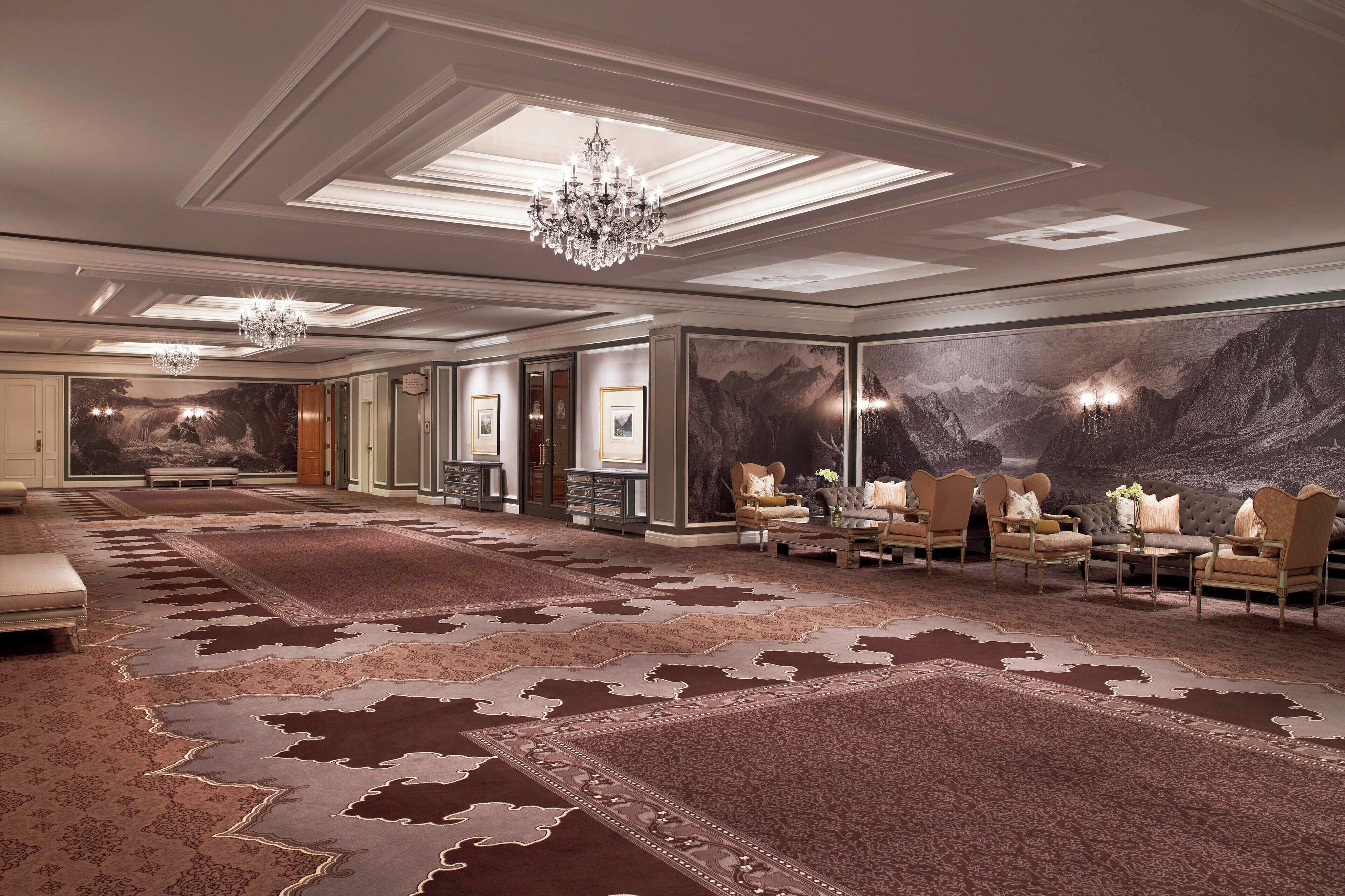 A spacious room with a large carpet, a chandelier, and a mountain mural on the wall.