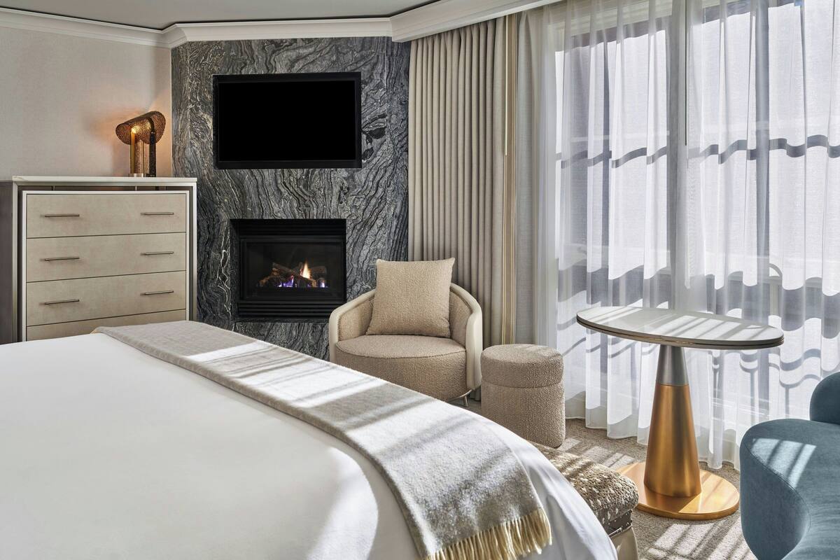 A modern hotel room with a bed, a fireplace, a television, a round table, and a chair.