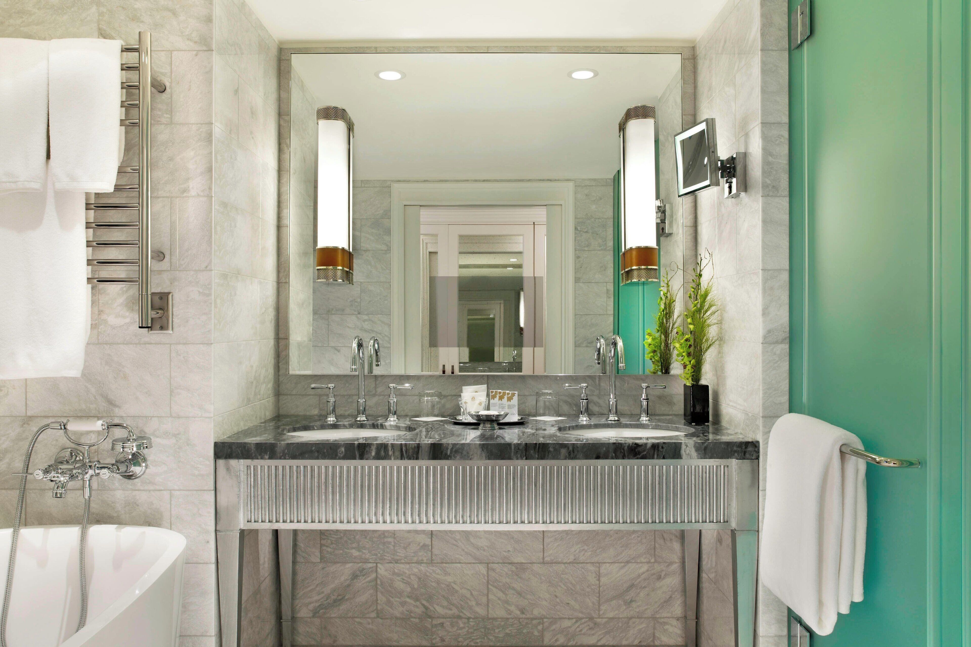 Un baño moderno con tocador de doble lavabo, una bañera independiente y un espejo grande con apliques de pared.
