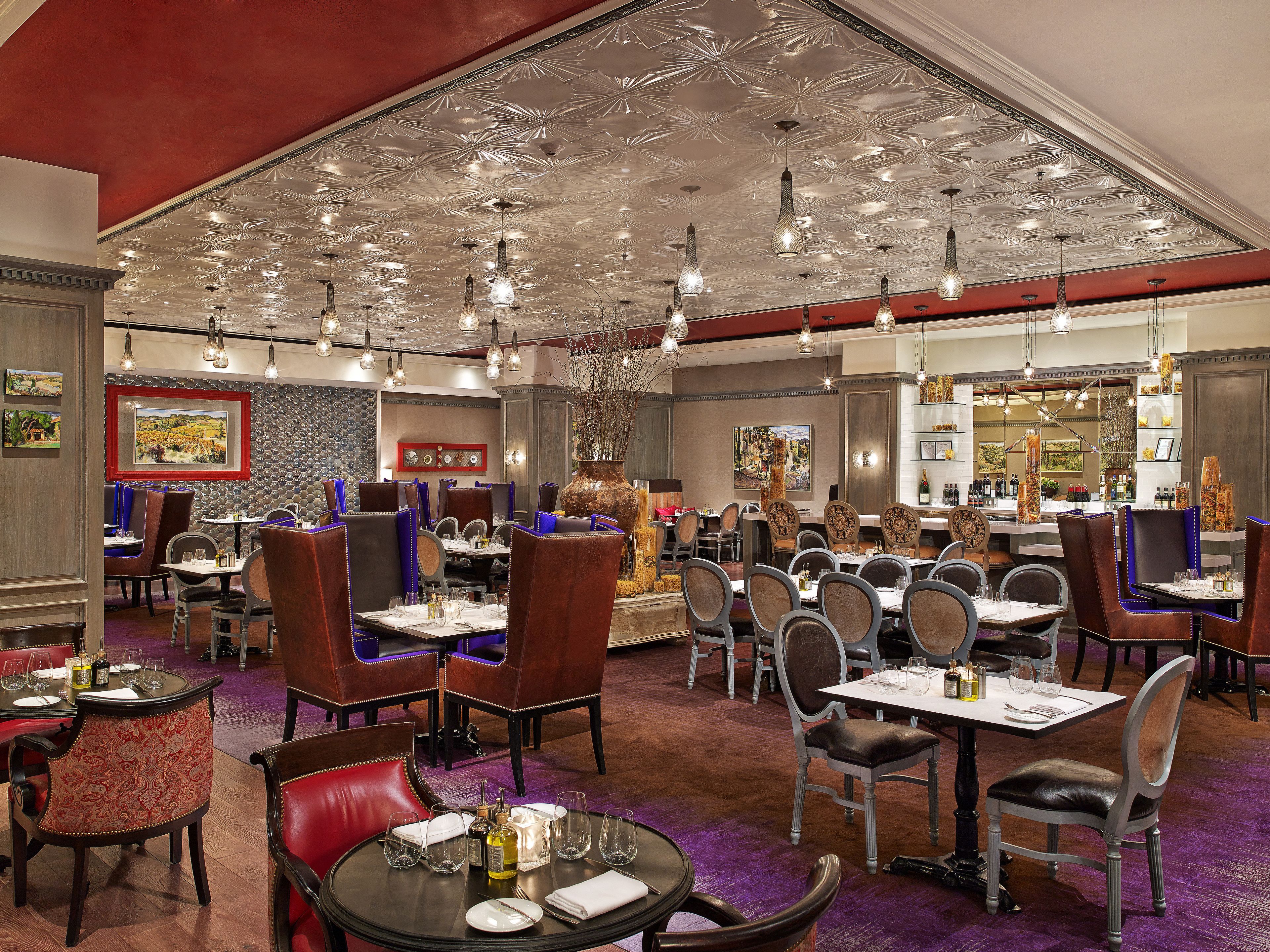 A restaurant with multiple dining tables and chairs, a decorative ceiling, and artwork on the walls.