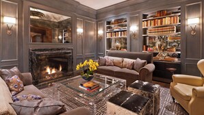 A sophisticated living room with a fireplace, leather sofas, a coffee table, and a bookshelf filled with books and decorative items. - The St. Regis Aspen Resort (Aspen)