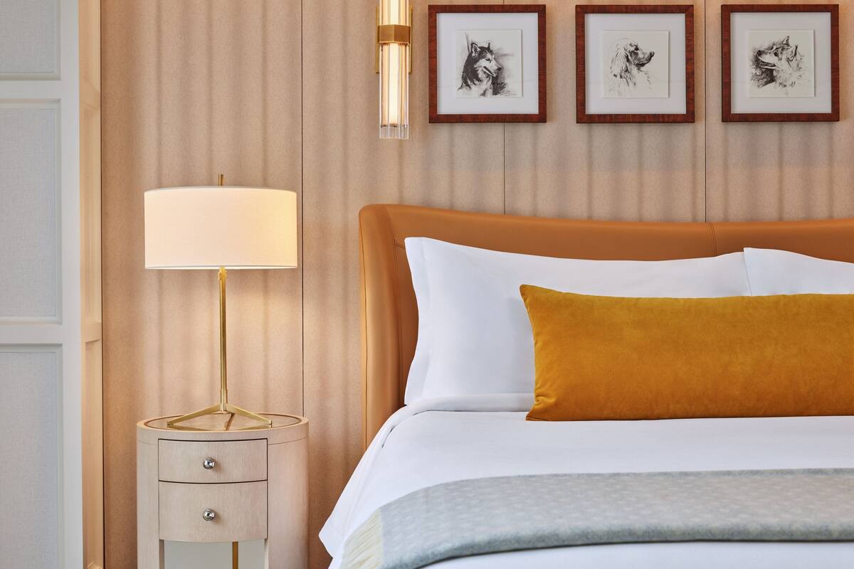 A neatly arranged bedroom with a bed, a bedside table with a lamp, and framed artwork on the wall.