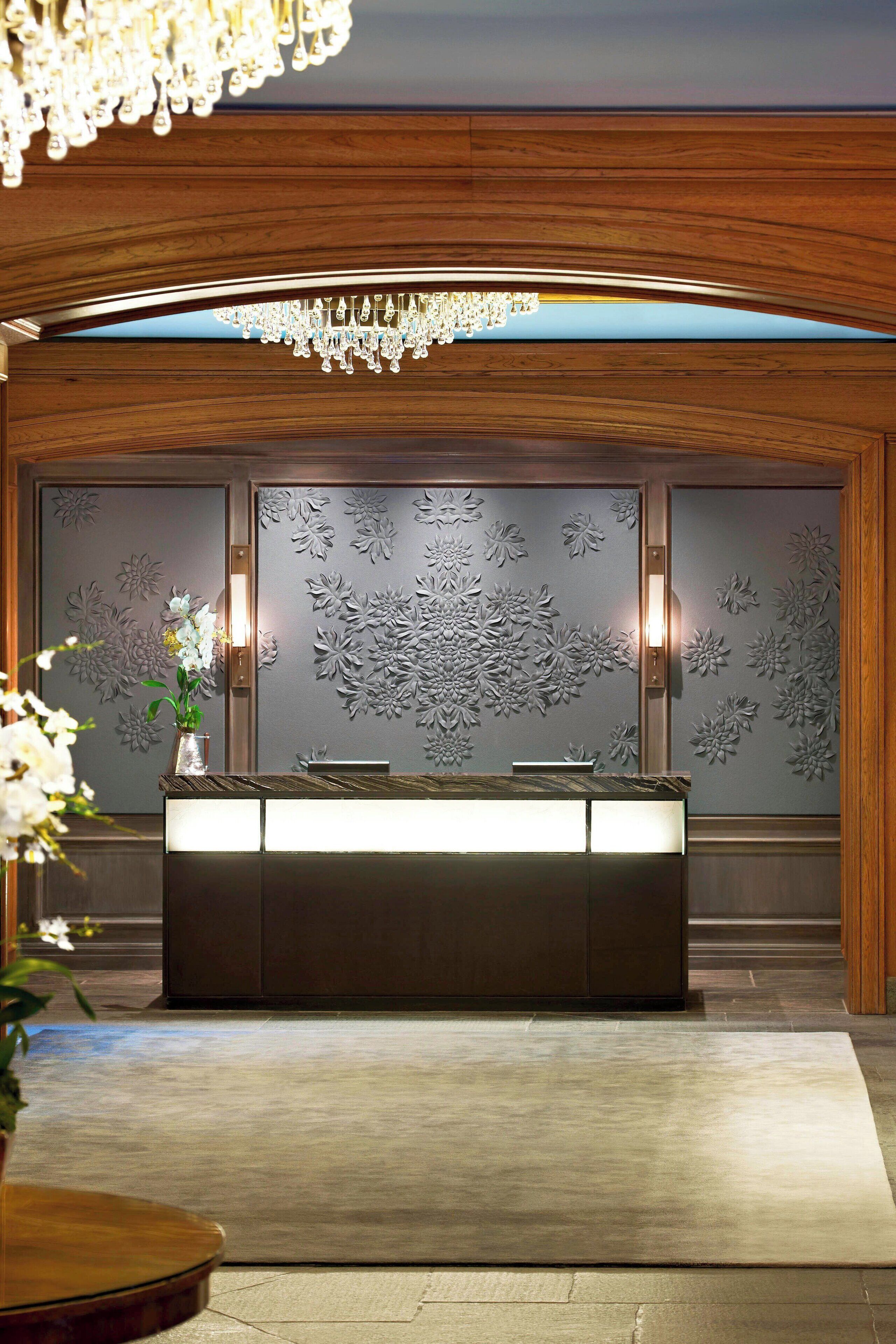 A reception area with a wooden reception desk, a chandelier, and a floral wall design.
